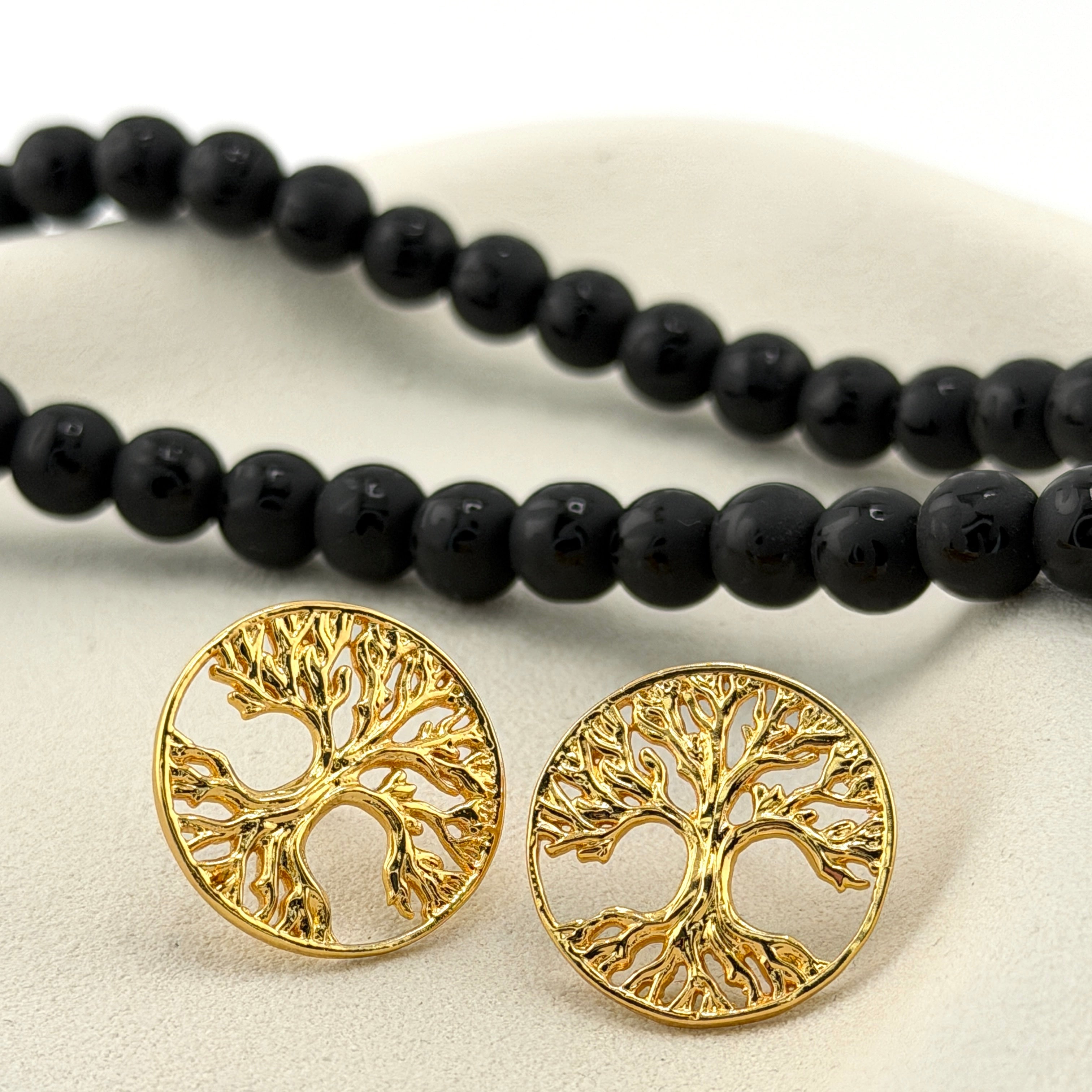 Gold tree-of-life earrings on a white surface with black beads.